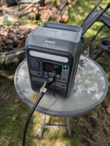 Anker SOLIX C300 portable power station on an outdoor camping table with a cable plugged in