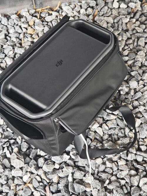 DJI Power 1000 V2 stored in a protective carrying case on gravel with a charging cable connected