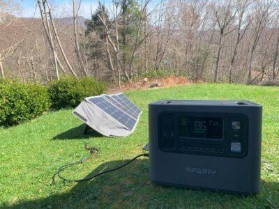 AFERIY P210 portable power station charging outdoors from a folding solar panel on a sunny lawn