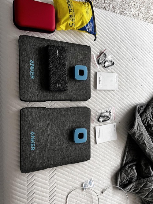 Two folded Anker SOLIX PS30 solar panels with their blue USB junction boxes, included carabiners, cables, and manuals laid out on a bed