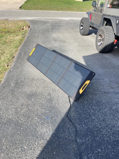 BougeRV FS200W portable solar panel propped on its kickstand on a driveway next to a Jeep with the charging cable running out to it