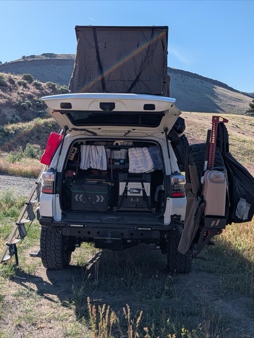 White 4Runner SUV with rooftop tent and gear set up at a hillside overland campsite where a BougeRV FS200W portable solar panel is used