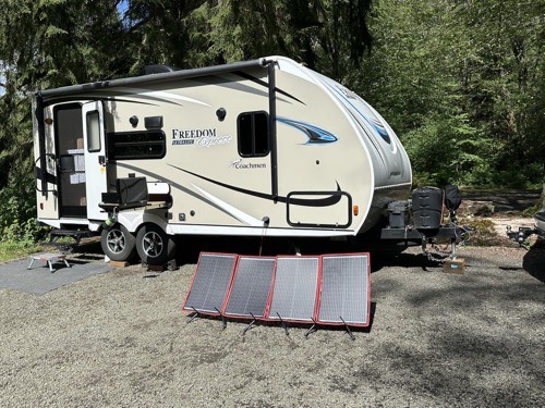 DOKIO 100W foldable solar panel kit set up on gravel in front of a Coachmen Freedom Express travel trailer at an RV campsite