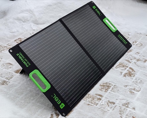 EBL 100W portable solar panel standing on its kickstand on snow-covered ground in winter sun