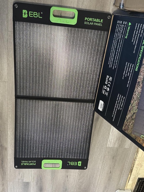 EBL 200W portable solar panel folded in half on a wood floor next to its retail box and spec sheet