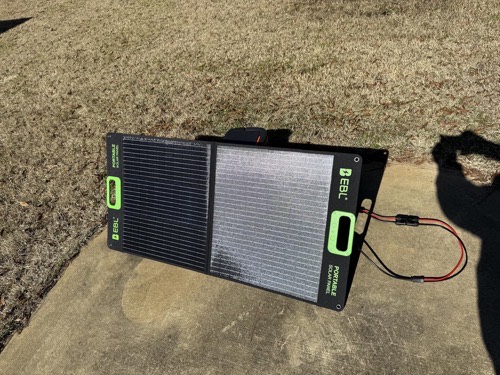 EBL 200W foldable solar panel propped open on a concrete pad over dry winter grass with the MC-4 charge cable attached