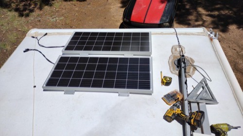 Two ECO-WORTHY 100W solar panels mounted side by side on an RV roof during installation with drill, tape measure, and speed square nearby