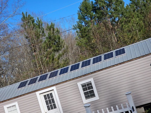 A row of ECO-WORTHY solar panels mounted on the metal roof of an off-grid cabin surrounded by pine trees