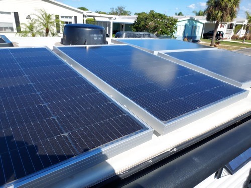 Four ECO-WORTHY 100W solar panels mounted flat on an RV roof in full sun at a mobile home park