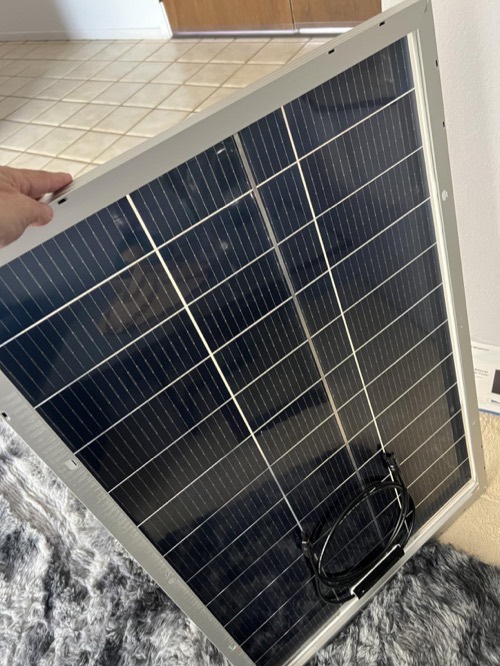 A person holding a single ECO-WORTHY 100W N-Type solar panel indoors, showing the anodized aluminum frame and MC4 cable lead