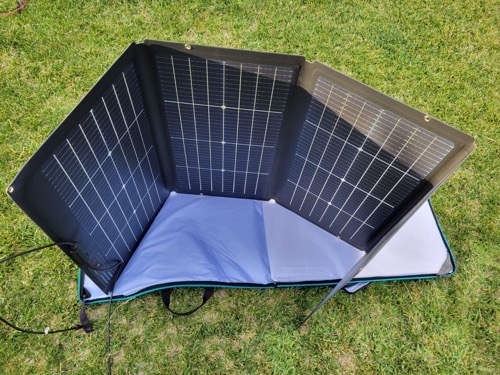 Rear view of the EcoFlow 220W bifacial solar panel on grass, showing the back-side cells and the case acting as a kickstand