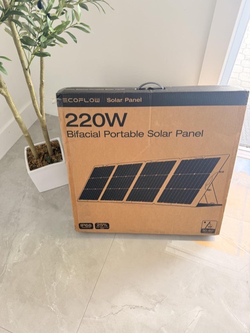 EcoFlow portable solar panel retail box standing on a tiled floor next to an indoor potted plant