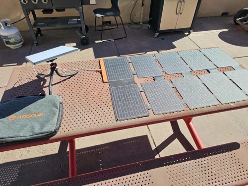 FlexSolar lx-S100 solar panel unfolded on a picnic table charging a white Starlink Mini dish in full sun