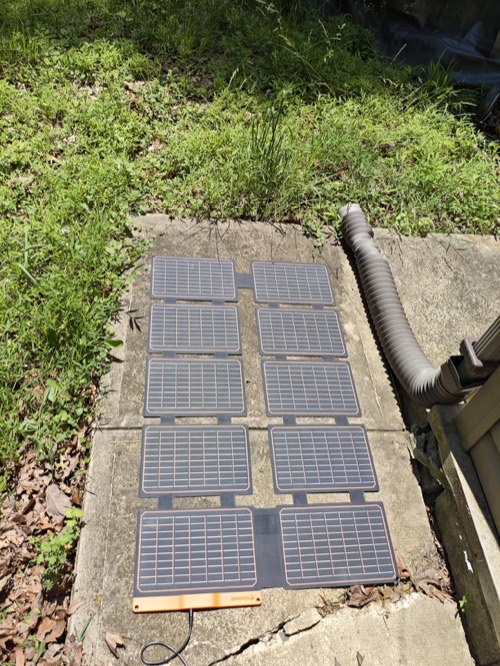 FlexSolar lx-S100 portable solar panel laid out on a concrete patio beside grass and a drain pipe in direct sun