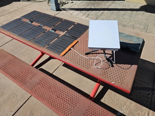 FlexSolar lx-S100 solar panel on a picnic table connected to a Starlink Mini and storage bag with DC cables