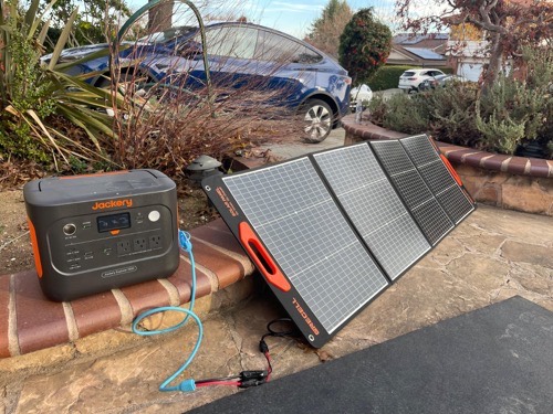 GRECELL SP-100 folding solar panel charging a Jackery power station on a stone patio with a car in the background