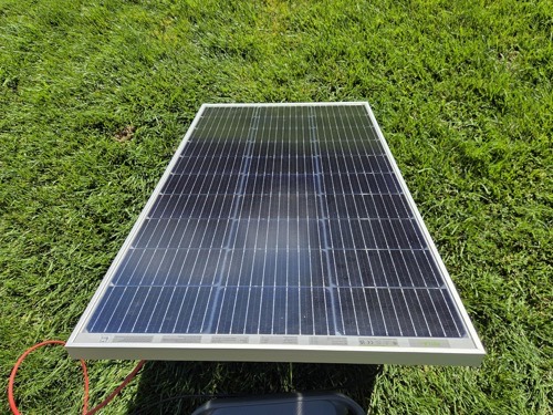 HQST 200W bifacial solar panel lying face-up on grass showing the dual-sided cell layout with an MC4 cable attached