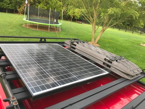 HQST 200W bifacial solar panel mounted on a vehicle roof rack next to recovery traction boards