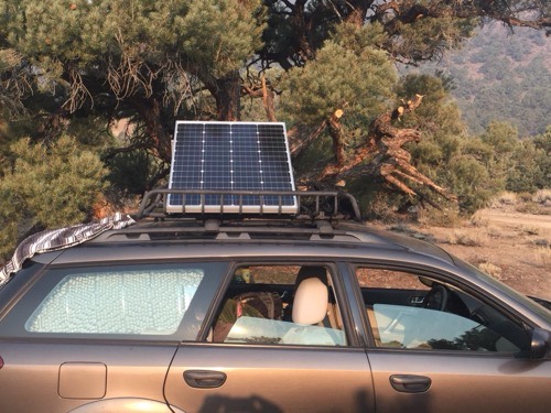 HQST bifacial 100W solar panel mounted in a roof basket on a station wagon parked in dry backcountry terrain