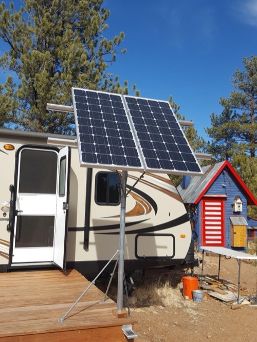 Two HQST bifacial 100W solar panels pole-mounted on a tilt rack beside an RV, raised with an air gap to catch reflected light