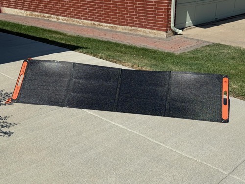 Jackery SolarSaga 200W bifacial solar panel unfolded flat on a driveway in front of a brick house in full sun