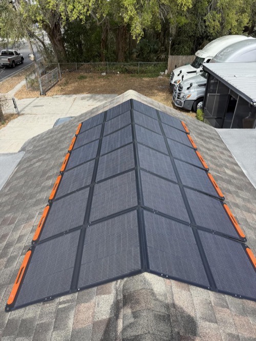 Two Jackery SolarSaga 200W bifacial solar panels mounted in a V layout on a shingled house roof with orange clips, vehicles parked below
