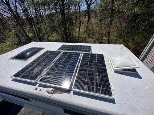Several Renogy 100W 12V solar panels laid out on a camper roof in a wooded area with MC4 leads connected