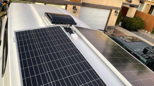 Two Renogy 100W solar panels installed side by side on a camper roof in a residential driveway