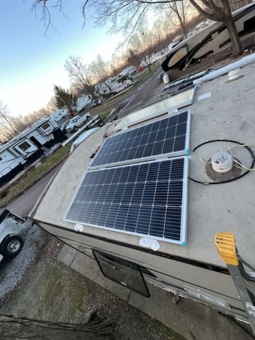 Two Renogy 100W solar panels mounted on an RV roof at a campground on a clear winter day