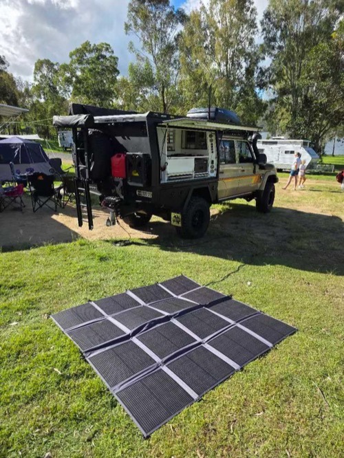 Renogy 400W solar panel blanket laid flat on grass beside an overland 4x4 truck camper at a campsite