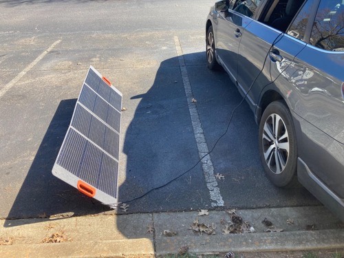 TWELSEAVAN 200W solar panel propped at a steep angle against a curb to charge a car in low winter sun in a parking lot