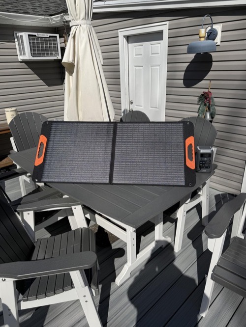 ZOUPW 100W portable solar panel unfolded on a patio table charging an orange portable power station in full sun