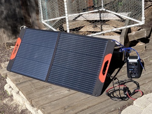 ZOUPW 100W solar panel deployed on kickstands in a backyard, connected by cable to a portable power station near a chicken coop